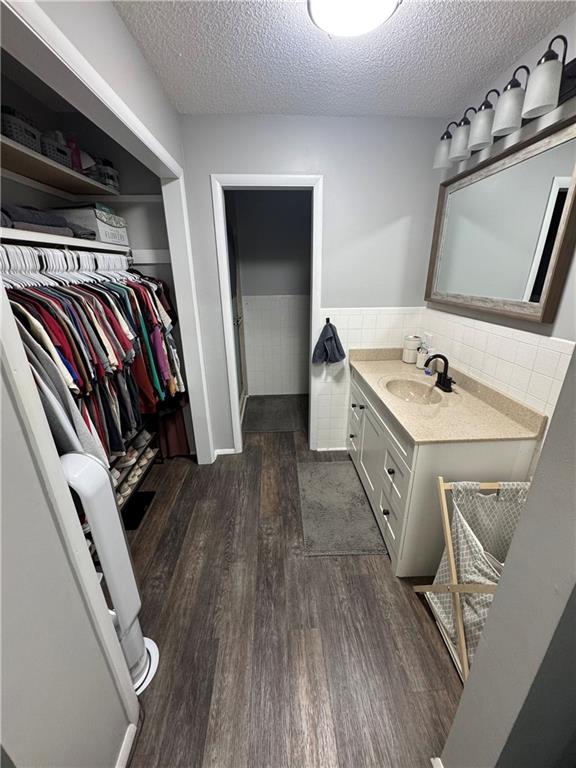 109 W 3rd St, Stanberry, MO 64489 - bathroom with vanity, wood finished floors, a walk in closet, a textured ceiling, and tile walls