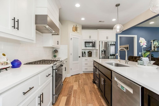 6614 Mccormick Dr, Shawnee, KS 66226 - kitchen with appliances with stainless steel finishes, range hood, light countertops, light wood finished floors, and pendant lighting