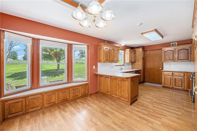 11180 Riverview Ave, Edwardsville, KS 66111 - kitchen with a peninsula, a chandelier, light wood finished floors, brown cabinetry, and decorative backsplash