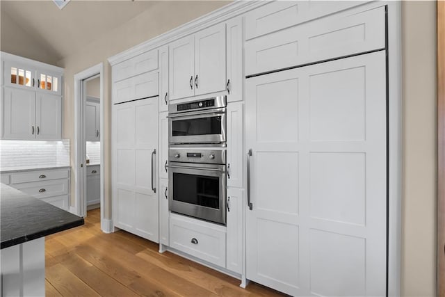 4915 NW Canyon Ct, Lees Summit, MO 64064 - kitchen with stainless steel double oven, white cabinets, light wood-style floors, vaulted ceiling, and glass insert cabinets