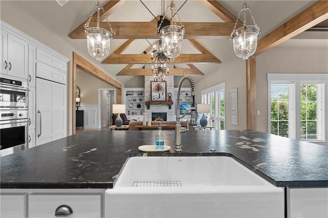 4915 NW Canyon Ct, Lees Summit, MO 64064 - kitchen with a stone fireplace, open floor plan, white cabinets, stainless steel double oven, and pendant lighting