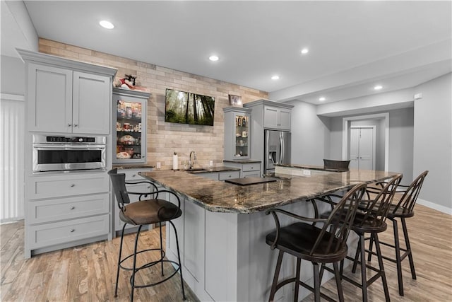 4915 NW Canyon Ct, Lees Summit, MO 64064 - kitchen with stainless steel appliances, a kitchen bar, light wood-style flooring, glass insert cabinets, and recessed lighting