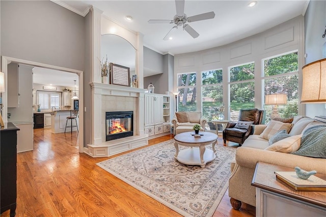 1617 Summit Valley Ln, Lees Summit, MO 64081 - living room featuring a ceiling fan, a tiled fireplace, light wood-style flooring, ornamental molding, and recessed lighting