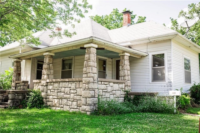 210 S Mulberry St, Paola, KS 66071 - view of side of home featuring covered porch, a chimney, stone siding, and a lawn