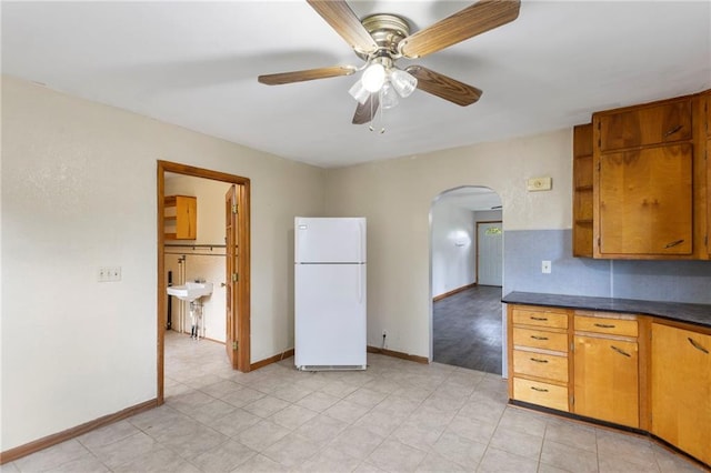 35365 Block Rd, Paola, KS 66071 - kitchen featuring freestanding refrigerator, arched walkways, dark countertops, ceiling fan, and brown cabinets