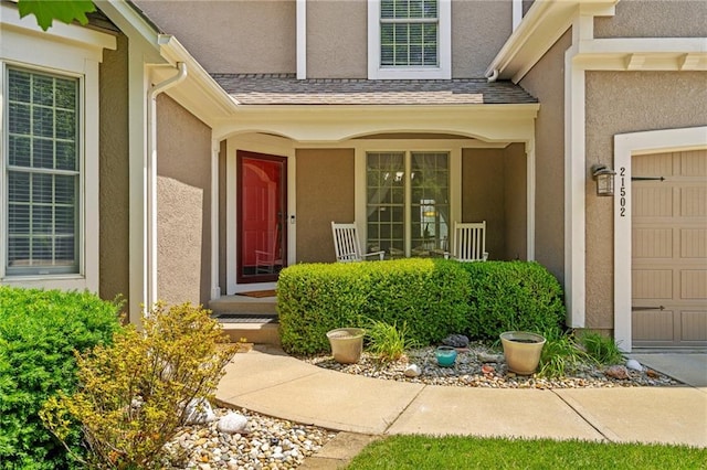 21502 W 98th Ter, Lenexa, KS 66220 - doorway to property featuring stucco siding, a porch, roof with shingles, and a garage