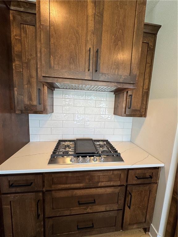 22415 87th Ter, Lenexa, KS 66227 - kitchen with stainless steel gas cooktop, decorative backsplash, exhaust hood, dark brown cabinets, and light stone countertops