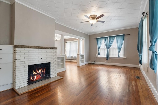 704 Lincoln St, Coffeyville, KS 67337 - unfurnished living room featuring a brick fireplace, hardwood / wood-style flooring, ceiling fan, crown molding, and decorative columns
