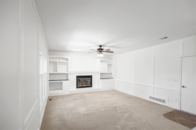 1467 E Orleans Dr, Olathe, KS 66062 - unfurnished living room with a decorative wall, ceiling fan, light carpet, a glass covered fireplace, and built in features