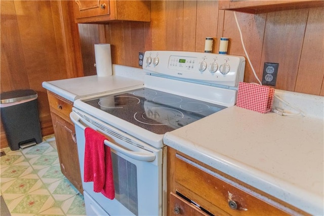 708 Osage St, Neodesha, KS 66757 - kitchen featuring white electric range oven, brown cabinets, light countertops, wooden walls, and light flooring