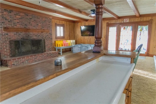 708 Osage St, Neodesha, KS 66757 - living room with wood walls, a fireplace, ornate columns, ceiling fan, and a wooden ceiling with exposed beams