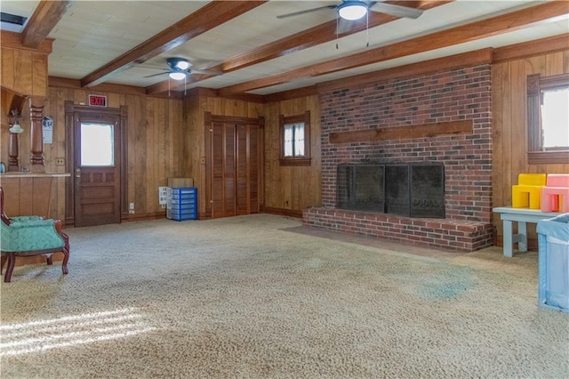 708 Osage St, Neodesha, KS 66757 - unfurnished living room with a ceiling fan, wood walls, beam ceiling, carpet floors, and a fireplace