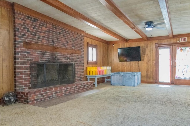 708 Osage St, Neodesha, KS 66757 - unfurnished living room featuring beamed ceiling, carpet flooring, wooden walls, a ceiling fan, and a brick fireplace