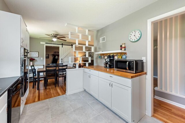 14224 E 36th St, Independence, MO 64055 - kitchen with stainless steel microwave, a barn door, wooden counters, black dishwasher, and a ceiling fan