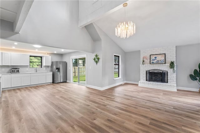 10312 W 48th Ter, Shawnee, KS 66203 - unfurnished living room with a chandelier, beam ceiling, high vaulted ceiling, light wood-type flooring, and a brick fireplace