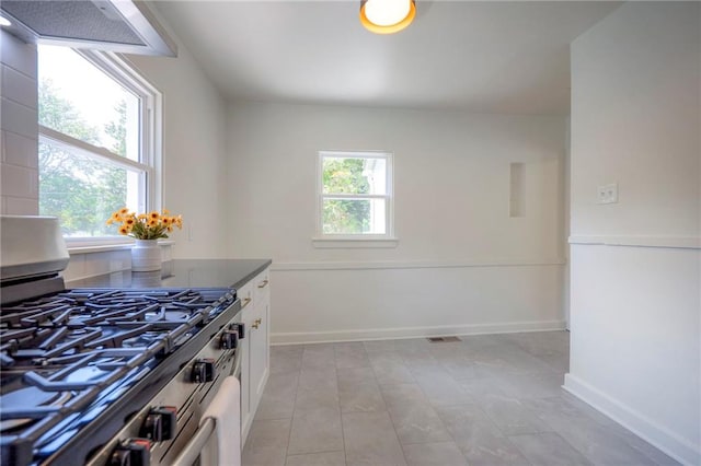 29 S 26th St, Kansas City, KS 66102 - kitchen with stainless steel gas stove, ventilation hood, white cabinets, and light tile patterned floors