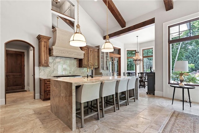 11110 W 146th Ter, Overland Park, KS 66221 - kitchen with stone tile flooring, tasteful backsplash, beamed ceiling, a kitchen island with sink, and a chandelier