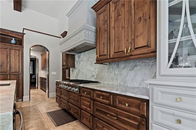 11110 W 146th Ter, Overland Park, KS 66221 - kitchen featuring stainless steel gas stovetop, backsplash, arched walkways, premium range hood, and light stone countertops