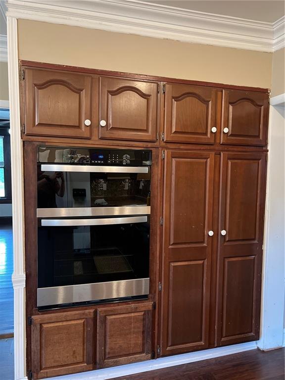 233 Main St, Osawatomie, KS 66064 - kitchen featuring double oven, ornamental molding, dark wood-style flooring, and brown cabinetry