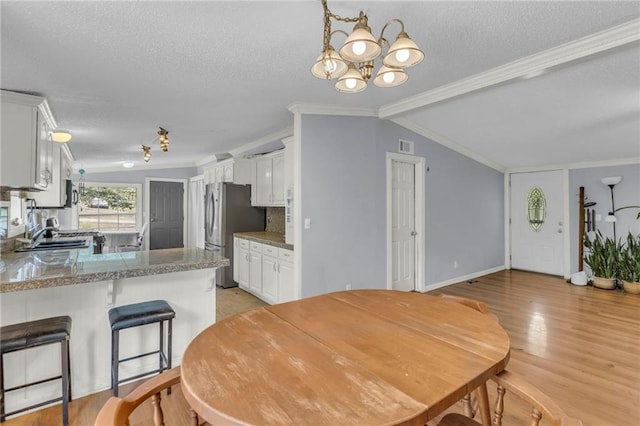 8036 Bellefontaine Ave, Kansas City, MO 64132 - dining area featuring a textured ceiling, ornamental molding, a chandelier, lofted ceiling, and light wood-style floors