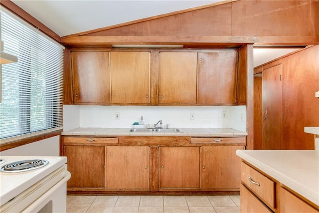 4400 N Brighton Ave, Kansas City, MO 64117 - kitchen with lofted ceiling, white electric range oven, light tile patterned floors, tile counters, and brown cabinets