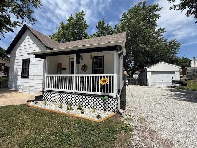 310 W 23rd St, Higginsville, MO 64037 - view of front of home with covered porch, a shingled roof, a detached garage, an outdoor structure, and gravel driveway