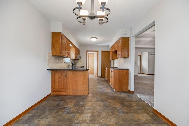 733 NE Colleen Dr, Lees Summit, MO 64086 - kitchen with dark countertops, brown cabinetry, decorative backsplash, a chandelier, and dark stone finish flooring