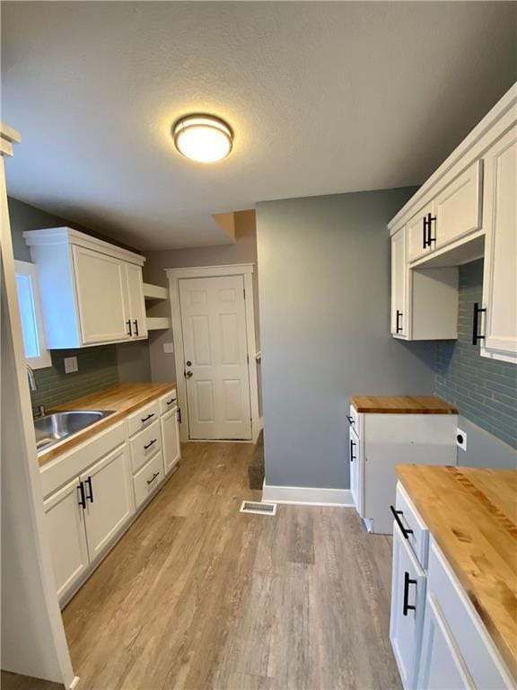 3046 N 27th St, Kansas City, KS 66104 - kitchen with wood counters, decorative backsplash, light wood finished floors, and white cabinets