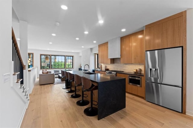 529 E 19th St, Kansas City, MO 64108 - kitchen featuring stainless steel appliances, dark countertops, light wood-style flooring, a kitchen island with sink, and a breakfast bar