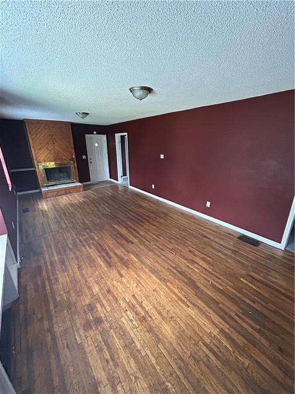 907 S Cedar Ave, Independence, MO 64052 - unfurnished living room with wood-type flooring, a textured ceiling, and a fireplace
