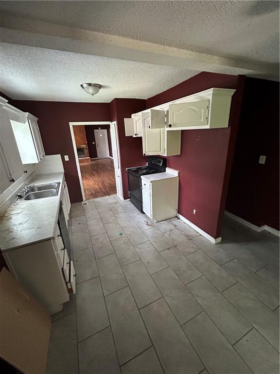 907 S Cedar Ave, Independence, MO 64052 - kitchen featuring black range oven, a textured ceiling, light countertops, light tile patterned floors, and white cabinets
