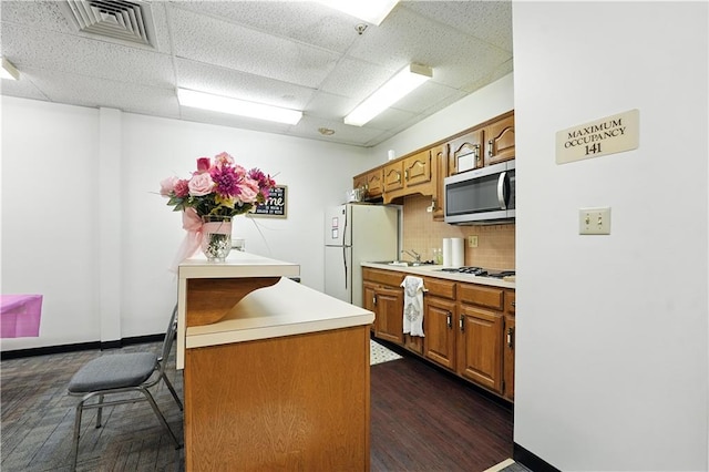 8001 Westridge Rd Unit 103, Raytown, MO 64138 - kitchen with white appliances, a drop ceiling, decorative backsplash, light countertops, and brown cabinetry