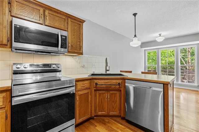 4116 NE 83rd St, Kansas City, MO 64119 - kitchen with appliances with stainless steel finishes, a peninsula, brown cabinets, light wood-style flooring, and light countertops