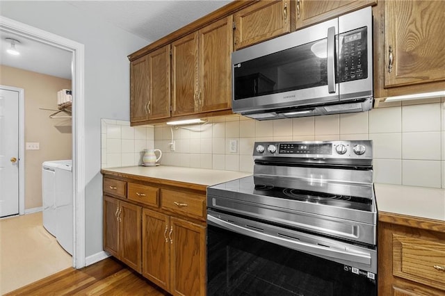 4116 NE 83rd St, Kansas City, MO 64119 - kitchen featuring appliances with stainless steel finishes, washing machine and clothes dryer, brown cabinetry, light countertops, and decorative backsplash