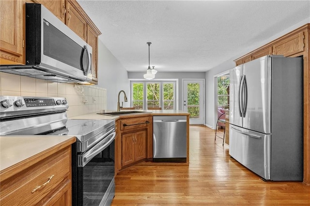 4116 NE 83rd St, Kansas City, MO 64119 - kitchen with stainless steel appliances, a peninsula, light wood-style flooring, brown cabinets, and a textured ceiling