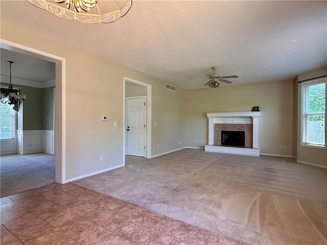 15598 S Blackfeather St, Olathe, KS 66062 - unfurnished living room with a chandelier, carpet, ceiling fan, a tiled fireplace, and a textured ceiling