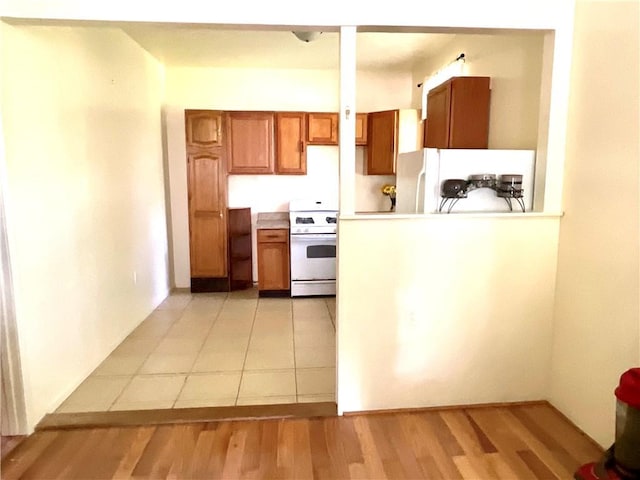 1870 N 27th St, Kansas City, KS 66104 - kitchen with white gas range, refrigerator, brown cabinets, light countertops, and light wood-type flooring