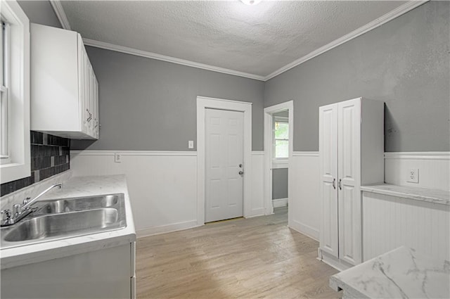 2524 Askew Ave, Kansas City, MO 64127 - kitchen with a textured ceiling, wainscoting, light wood finished floors, white cabinets, and ornamental molding