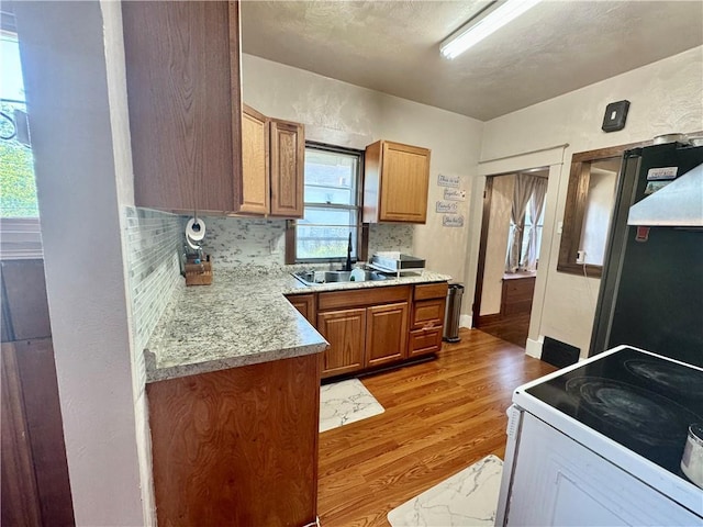144 N Brighton Ave, Kansas City, MO 64123 - kitchen with white range with electric cooktop, light wood-style flooring, light countertops, brown cabinetry, and backsplash