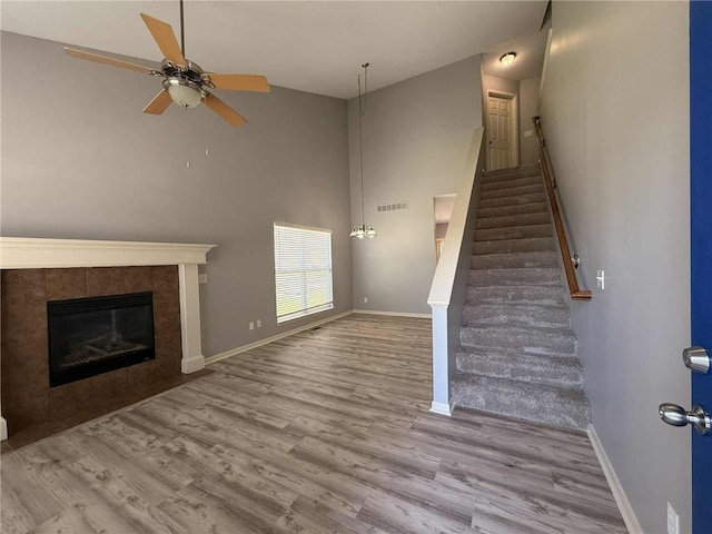8808 NE 97th St, Kansas City, MO 64157 - unfurnished living room featuring wood finished floors, ceiling fan, stairway, a tiled fireplace, and a towering ceiling