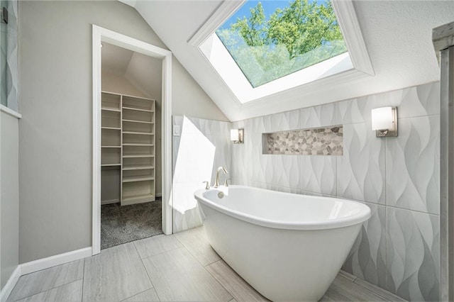 109 NE Locust St, Blue Springs, MO 64014 - bathroom with lofted ceiling, a freestanding bath, a skylight, a walk in closet, and tile walls