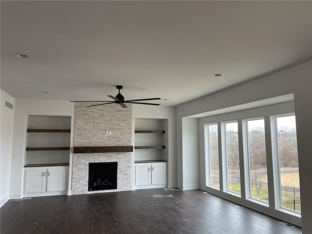 9015 N Colorado Ave, Kansas City, MO 64156 - unfurnished living room featuring built in features, a ceiling fan, a stone fireplace, and dark wood-style flooring