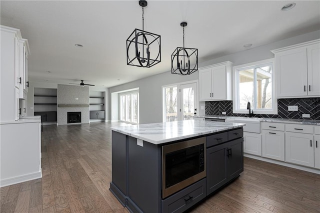 9015 N Colorado Ave, Kansas City, MO 64156 - kitchen featuring stainless steel microwave, white cabinetry, ceiling fan, tasteful backsplash, and decorative light fixtures