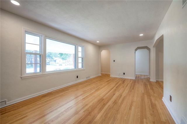 6605 Willow Ave, Raytown, MO 64133 - empty room featuring arched walkways, light wood-type flooring, a textured ceiling, and recessed lighting