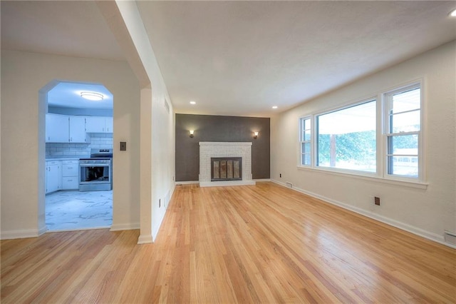6605 Willow Ave, Raytown, MO 64133 - unfurnished living room with a brick fireplace, light wood-type flooring, recessed lighting, and arched walkways