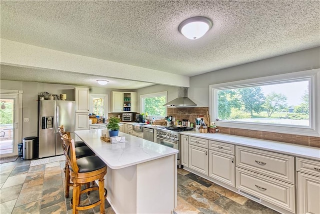 440 41p Rd, Clinton, MO 64735 - kitchen with appliances with stainless steel finishes, wall chimney range hood, a textured ceiling, stone tile floors, and a kitchen island