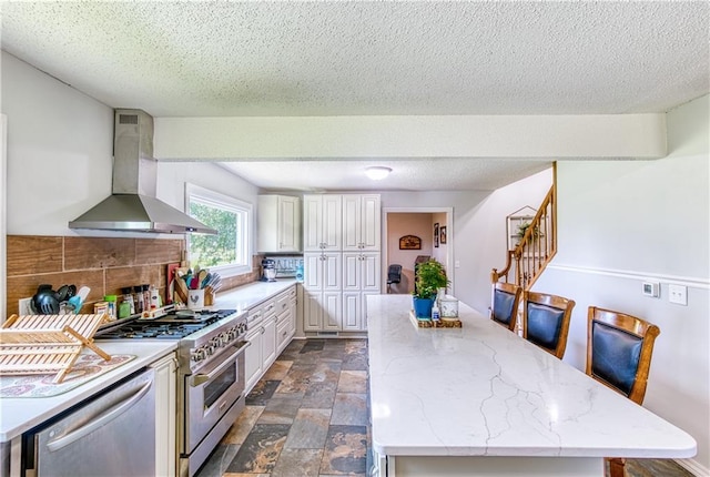 440 41p Rd, Clinton, MO 64735 - kitchen with wall chimney range hood, stainless steel appliances, a kitchen island, white cabinets, and a textured ceiling