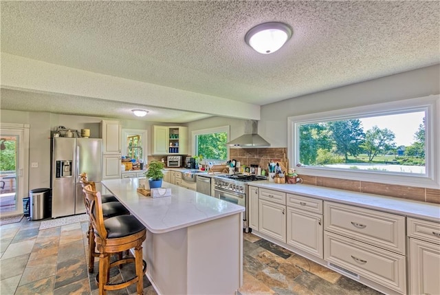 440 41p Rd, Clinton, MO 64735 - kitchen featuring stainless steel appliances, wall chimney range hood, a textured ceiling, stone tile floors, and a center island