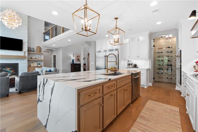 23717 W 118th Ter, Olathe, KS 66061 - kitchen featuring stainless steel appliances, a fireplace, white cabinets, a chandelier, and light wood-style flooring