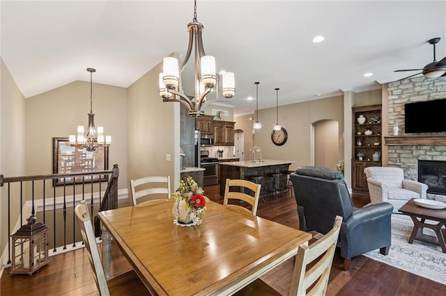 1415 SW Antiquity Dr, Lees Summit, MO 64081 - dining room featuring a chandelier, a ceiling fan, arched walkways, a stone fireplace, and dark wood-style flooring